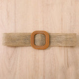 Natural woven belt with square wooden buckle on light wooden background.