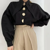 Chic black shirt with pearl-button detail, styled with cream trousers, showcasing Y2K fashion.