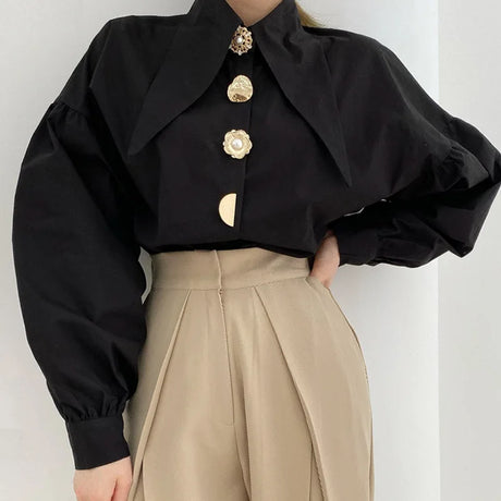 Chic black shirt with pearl-button detail, styled with cream trousers, showcasing Y2K fashion.