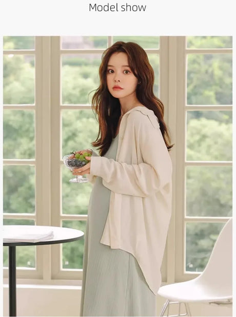 Model showcasing a sleeveless maternity dress with a light cardigan, set in a bright outdoor setting.