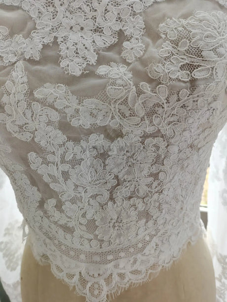 Detailed lace design of a bridal wrap jacket showcasing intricate floral appliques on a soft polyester fabric.