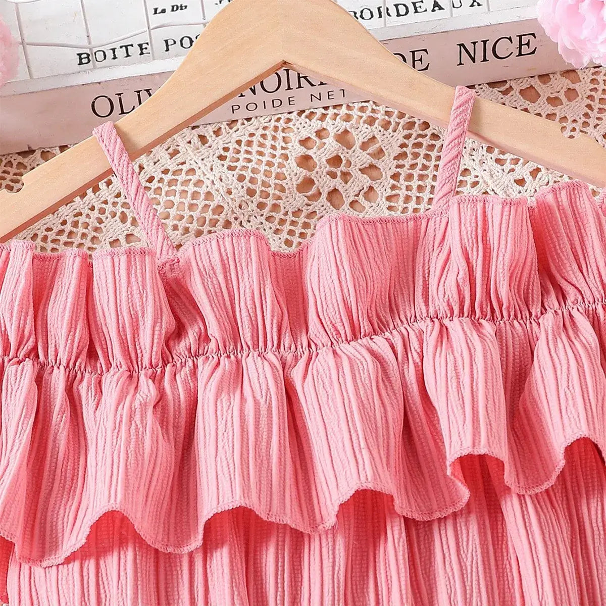 Girls casual summer dress with one-line shoulder straps and ruffled pink design on a hanger.