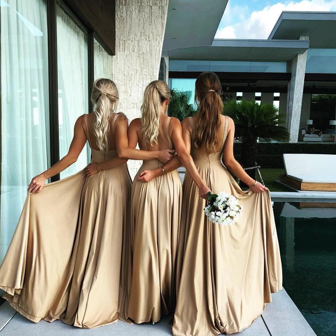 Three bridesmaids in sleeveless V-neck evening dresses, holding skirts, showcasing a flowy satin design.