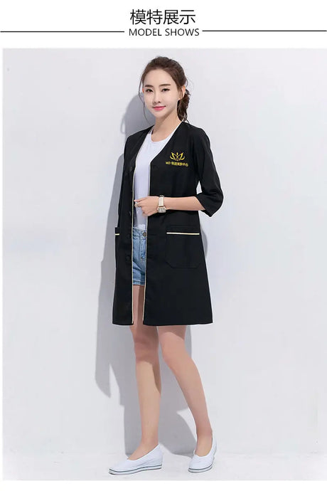 Model wearing a black salon beauty lab coat, showcasing pockets and stylish design, perfect for beauty professionals.