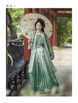 Women’s Hanfu cosplay featuring a beautiful green dress and floral parasol in a serene outdoor setting.