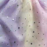 Close-up of shimmering star-patterned mesh fabric in pastel purple and cream colors for children's dress.