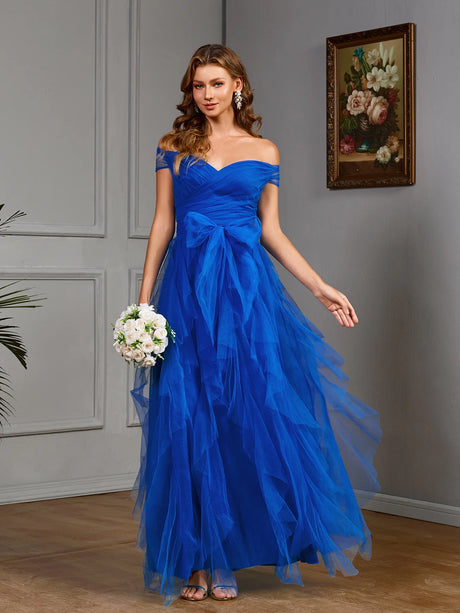 Elegant blue off-the-shoulder gown with layered tulle and floral bouquet in a stylish indoor setting.