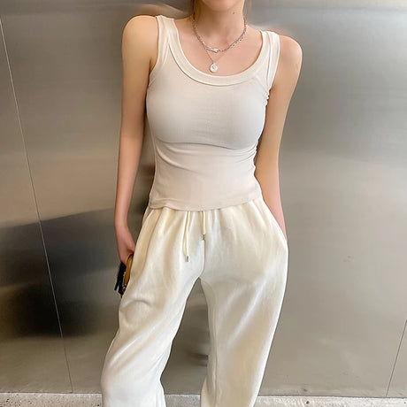 Model wearing a sleeveless cream ribbed tank top paired with white jogger pants, showcasing a casual streetwear look.