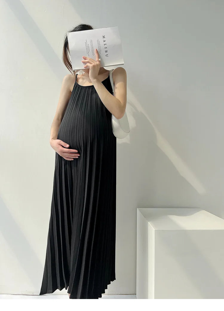 Pregnant woman in a pleated black maternity dress posing with a book in a bright setting.