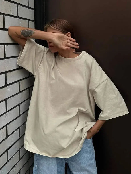 Woman wearing oversized beige casual t-shirt against a brick wall, showcasing comfort and style.