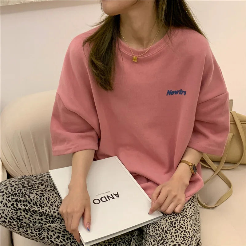 Oversized Harajuku streetwear tee in pink, worn casually with a notebook, showcasing relaxed fit and comfortable style.