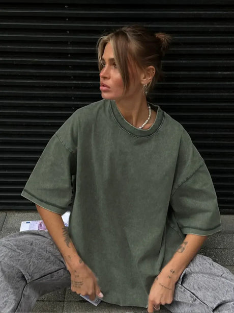 Woman wearing a loose-fit, casual green oversized t-shirt, sitting stylishly against a black backdrop.