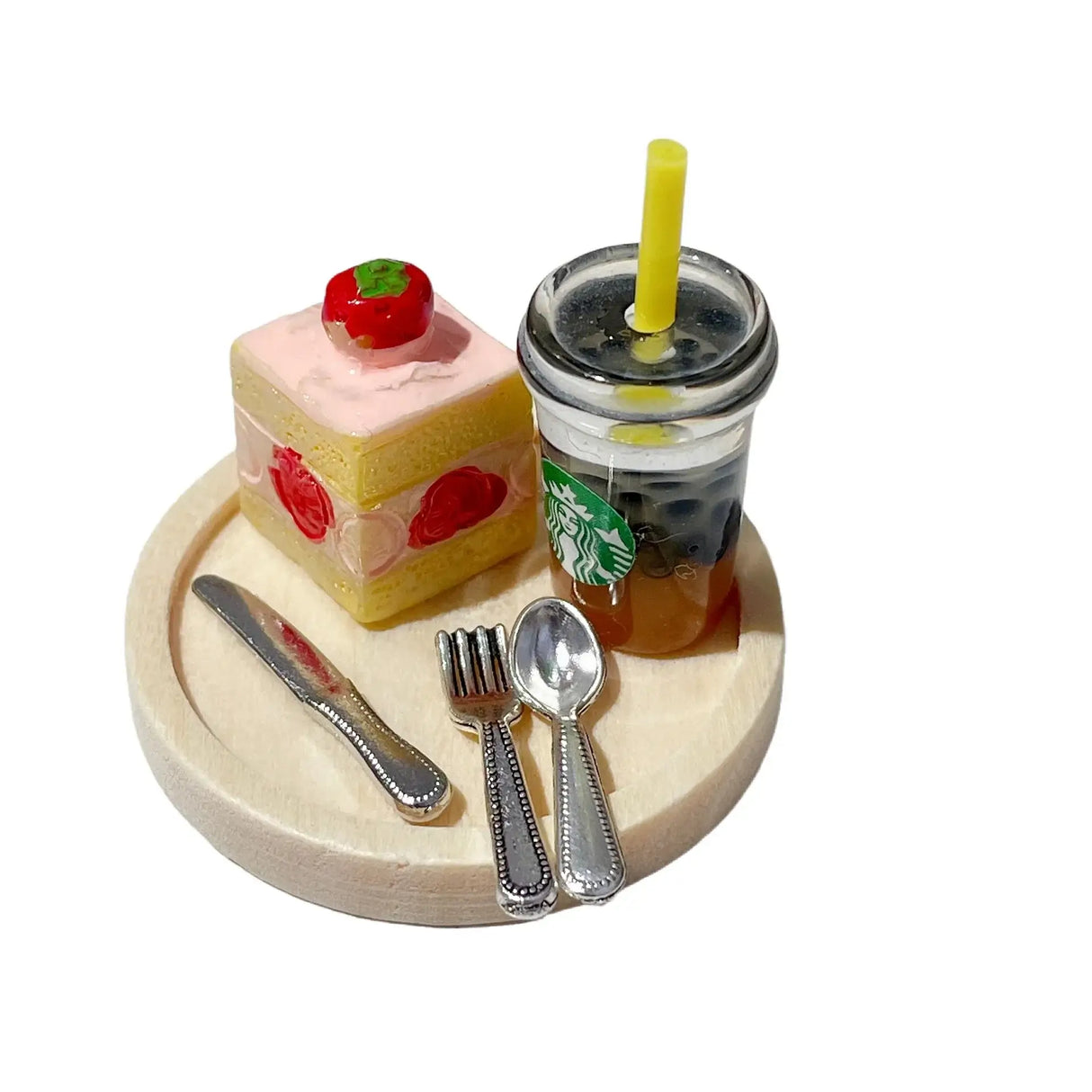 Miniature dessert set featuring a cake and Starbucks drink on a wooden plate with utensils.