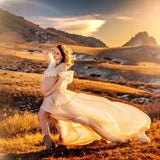 Pregnant woman in a flowing boho dress posing in a scenic outdoor setting, showcasing maternity style.