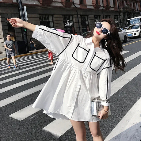 Woman wearing a stylish white maternity shirt dress with pockets, posing on a city street, perfect for summer outings.