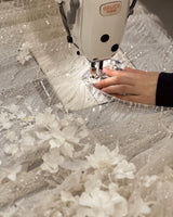 Close-up of a sewing machine creating a detailed bridal gown with floral and sequined embellishments.