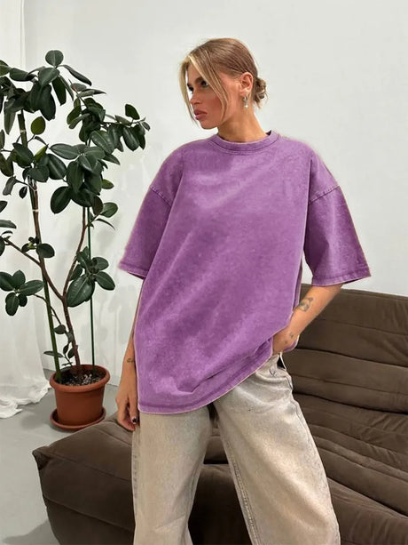 Woman wearing a loose-fitting purple casual t-shirt, styled with light-colored baggy pants in a minimalist indoor setting.