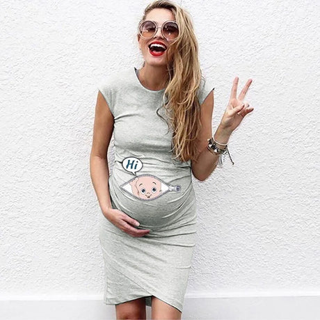 Smiling woman in a grey loose maternity dress with cartoon baby design, posing happily outdoors.