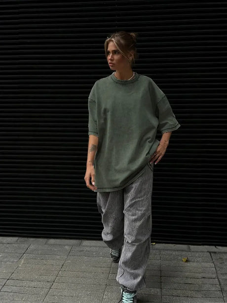 Woman in oversized green casual T-shirt and striped pants walking outdoors against a dark background.