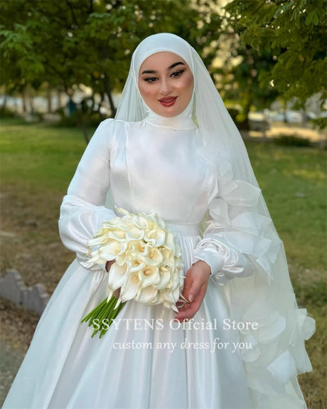 Bridal model in a Muslim A-Line satin wedding dress, holding white flowers in an outdoor setting.
