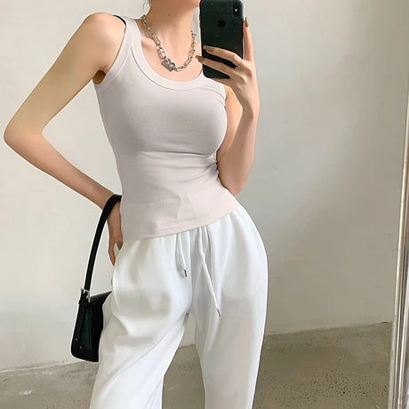 Model wearing a sleeveless nude ribbed tank top with white sweatpants, showcasing trendy streetwear style.