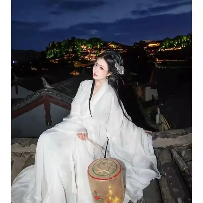 Elegant woman in traditional white Hanfu dress sitting on rooftop at night with lantern, showcasing Chinese cultural beauty.