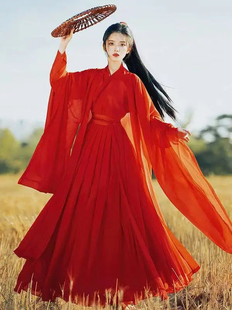 Woman in flowing wine red Hanfu costume with traditional fan, showcasing Tang Dynasty style elegance in a natural setting.