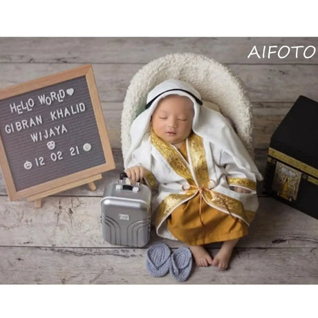 Infant boy dressed in a traditional outfit with a mini suitcase, showcasing BABI Boy Clothes creative design.