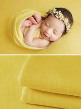 Newborn wrapped in yellow soft blanket with floral headband, ideal for photography and cozy moments.