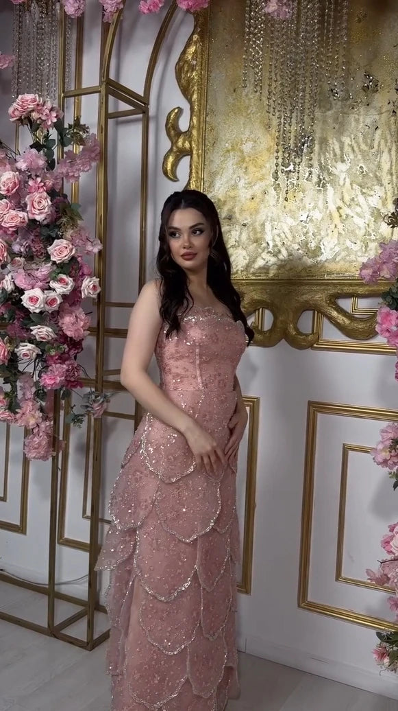 Model wearing a customized pink beaded engagement dress with a tiered skirt, surrounded by floral decorations.
