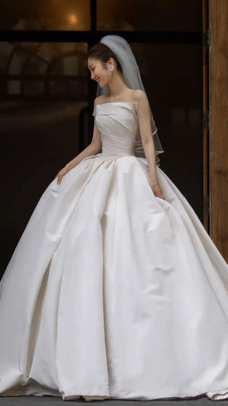 Bride in elegant satin wedding dress with off-shoulder design and full skirt, showcasing timeless bridal fashion.