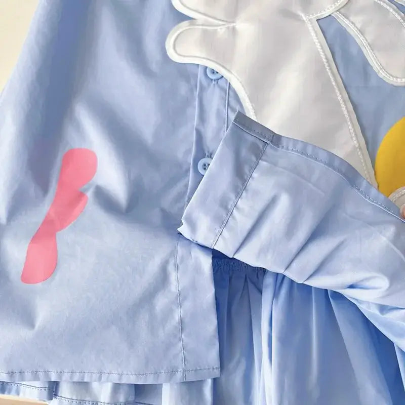 Close-up of a light blue girls summer dress featuring colorful cartoon patches and a turn-down collar.