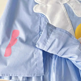 Close-up of a light blue girls summer dress featuring colorful cartoon patches and a turn-down collar.