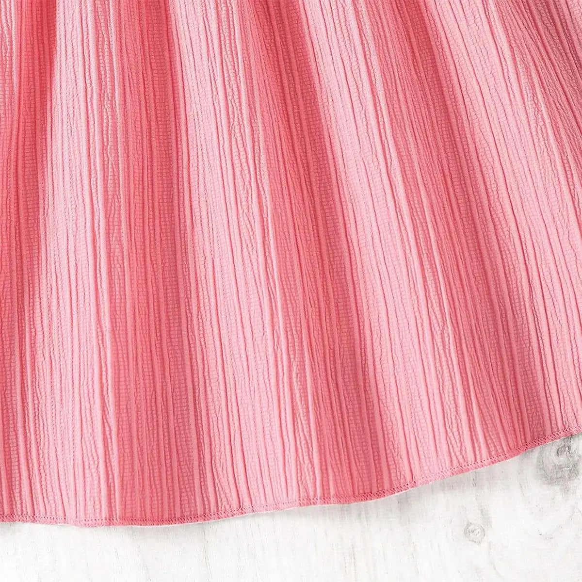 Close-up of a textured pink fabric, showcasing the soft pleats, ideal for girls' casual dresses.