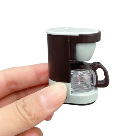 Miniature resin coffee maker prop held in hand, perfect for newborn baby photography and creative setups.