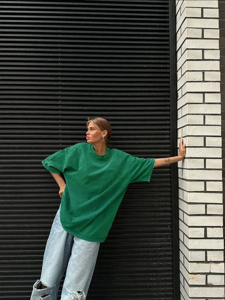 Woman wearing a green oversized casual t-shirt against a textured wall, styled with loose jeans.