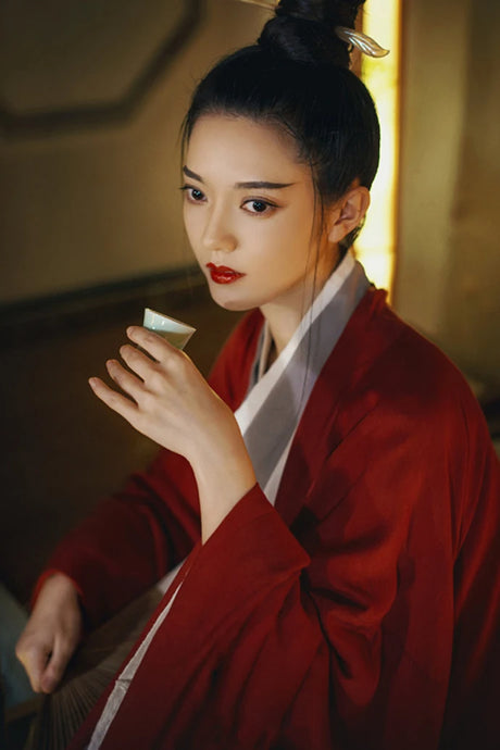 Woman in traditional wine red Hanfu holding a tea cup, showcasing Tang Dynasty elegance and style.