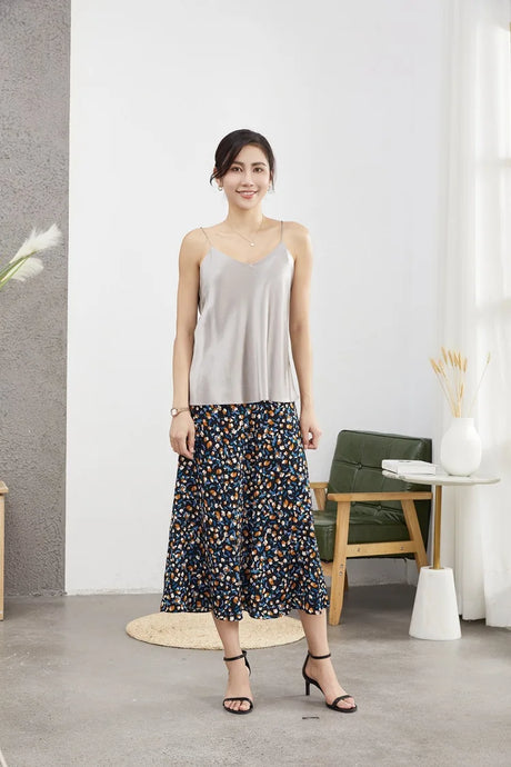 Woman wearing a stylish gray camisole and floral skirt in a modern interior, showcasing summer fashion.