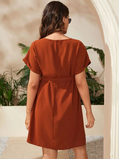 Woman wearing a bat-sleeve maternity tunic dress in burnt orange, showcasing a knee-length design and elegant style.