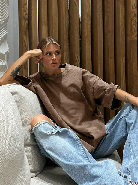 Model wearing a casual brown oversized t-shirt, styled with ripped jeans in a modern indoor setting.