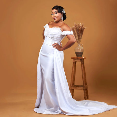 Elegant off-shoulder wedding dress adorned with pearls, featuring a detachable train and a stylish mermaid fit.