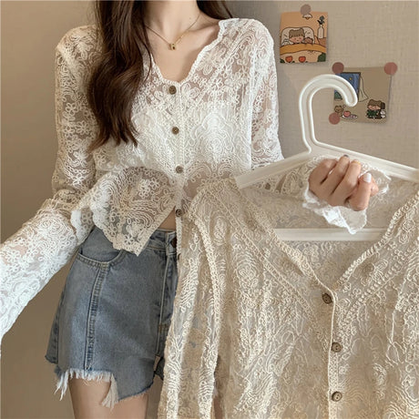 Woman holding a sheer lace sun shirt on a hanger, showcasing its intricate pattern and stylish design.