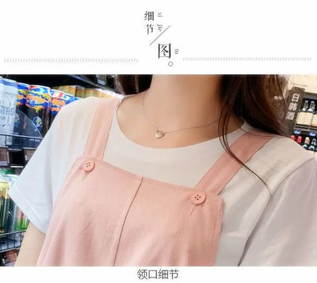 Close-up of a woman wearing a pink overall dress over a white shirt, showcasing a heart necklace.