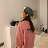 Profile view of a woman wearing a pink oversized Harajuku streetwear tee and a gray beret in a cozy indoor setting.