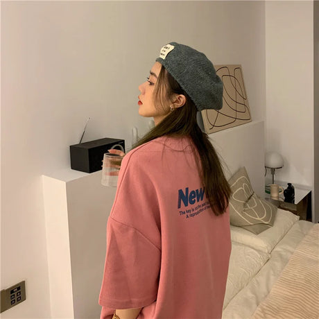 Profile view of a woman wearing a pink oversized Harajuku streetwear tee and a gray beret in a cozy indoor setting.