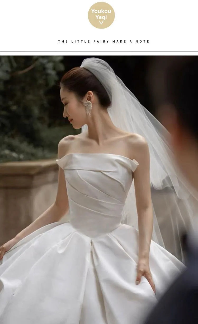 Elegant bride in a strapless satin wedding gown with a flowing veil, showcasing a classic bridal look.