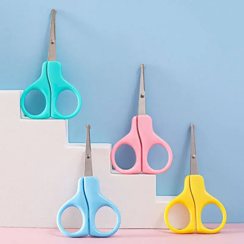 Colorful baby nail scissors in blue, pink, and yellow on a light background for safe grooming.