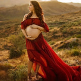 Pregnant woman in a boho two-piece maternity set, posing outdoors in a beautiful red dress at sunset.