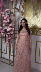 Elegant woman in a pink beaded engagement gown with a tiered skirt, posed in front of floral decor.
