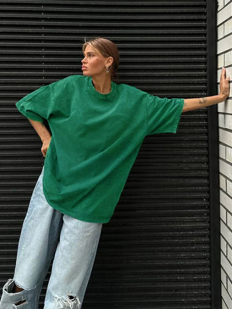Woman wearing a loose-fitting green casual t-shirt with oversized sleeves against a textured wall.